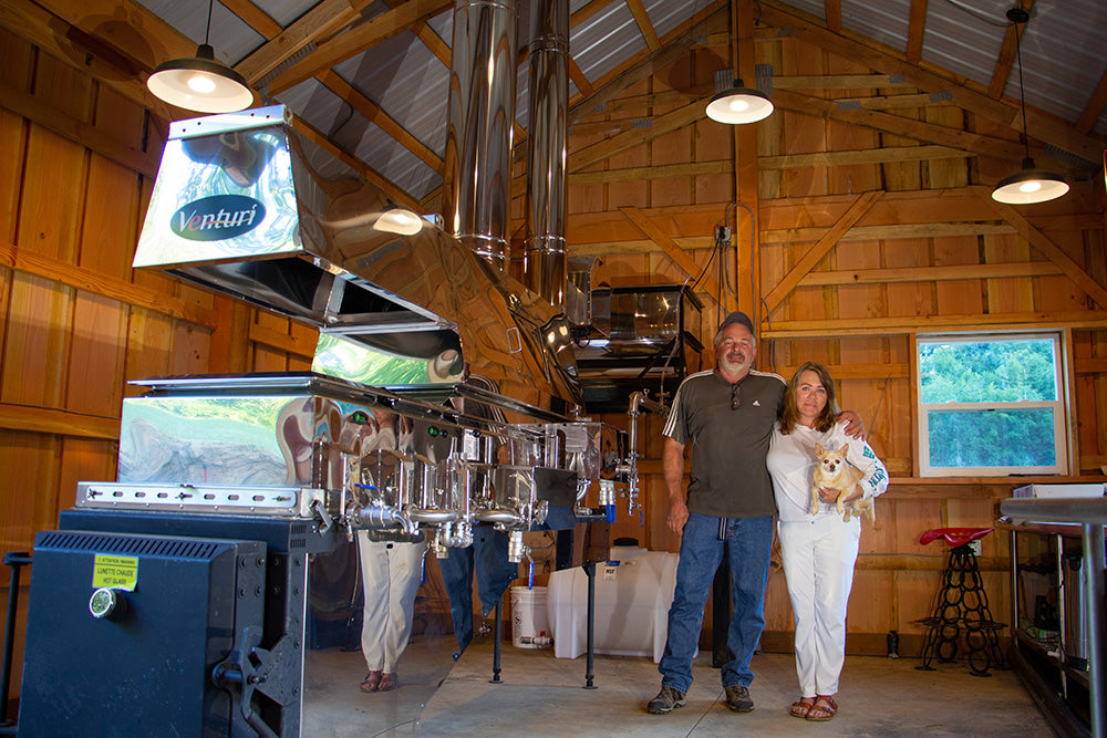 Connie, Dean, and their dog Zoe standing the bigleaf maple syrup sugar shack.